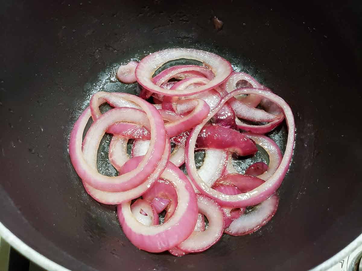 red onions sliced into rings cooking in a pan for Chicken Spinach Sandwiches.