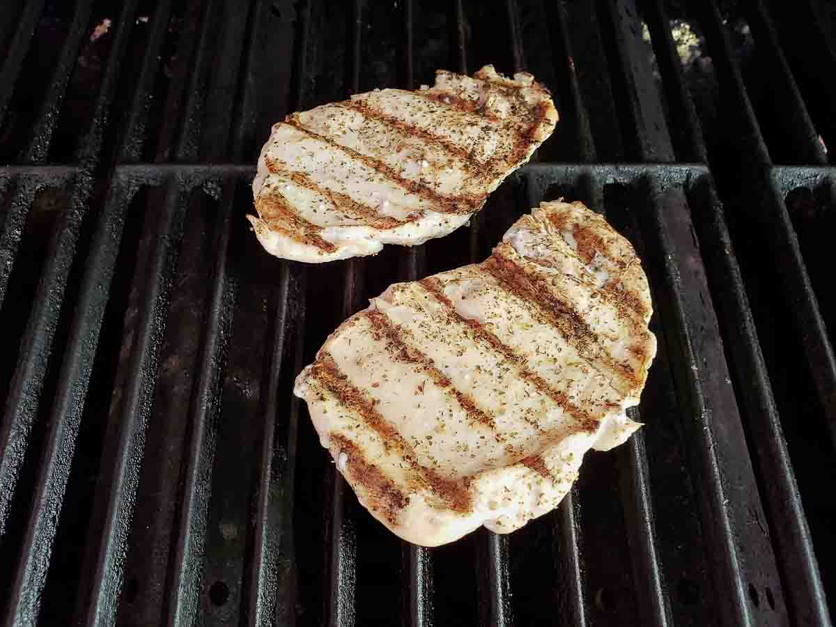 two chicken breasts cooking on a grill.