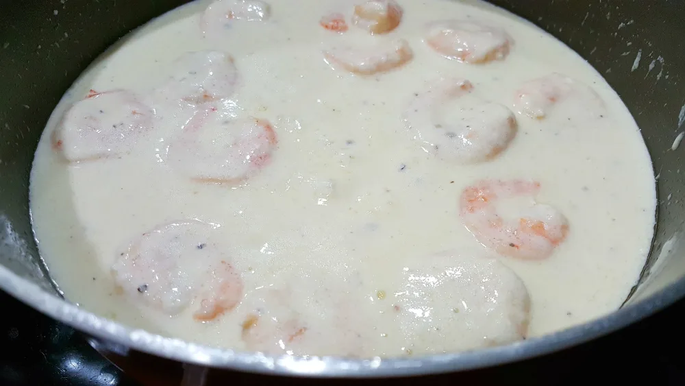 shrimp and alfredo sauce cooking in a pan