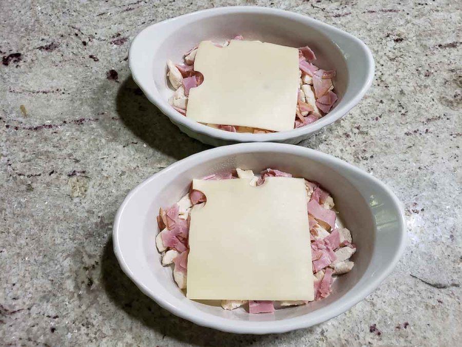 sliced swiss cheese layered over ham and chicken in baking dishes
