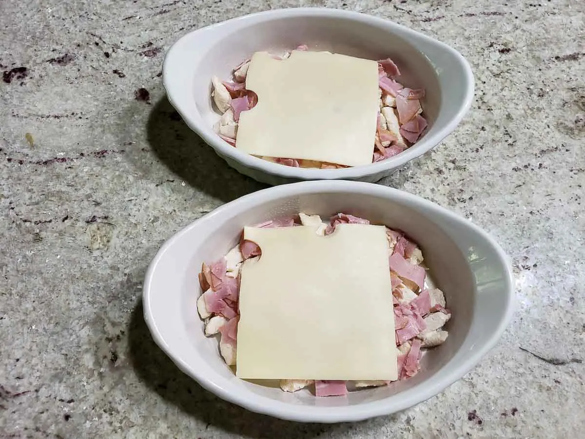 sliced swiss cheese layered over ham and chicken in two dishes.