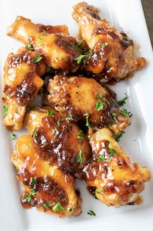 Sweet and Sour Sticky Wings sprinkled with parsley on a white platter