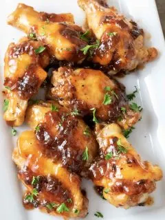 Sweet and Sour Sticky Wings sprinkled with parsley on a white platter
