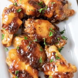 Sweet and Sour Sticky Wings sprinkled with parsley on a white platter