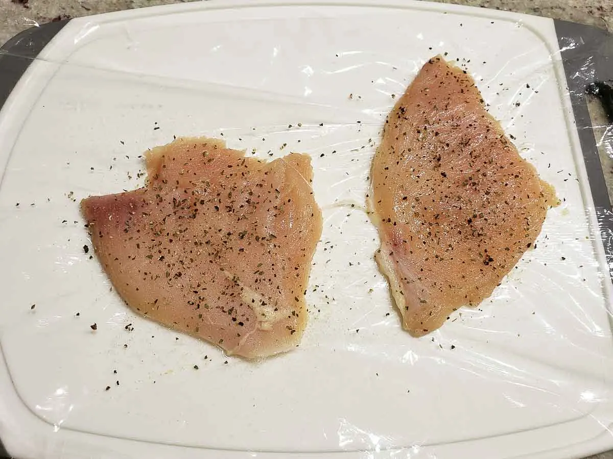 two chicken cutlets pounded flat and sprinkled with seasonings.