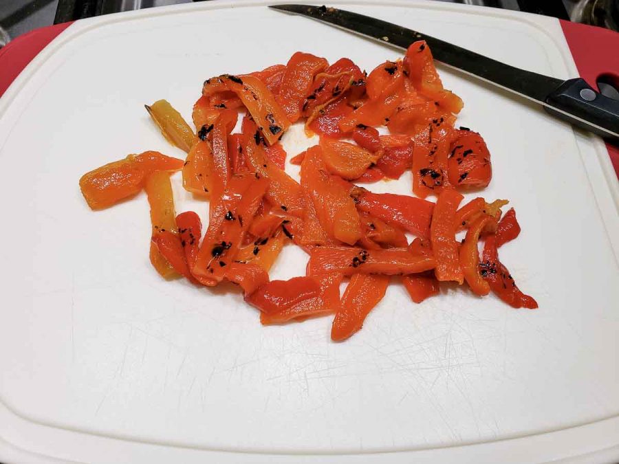 roasted red peppers sliced on a cutting board with a knife
