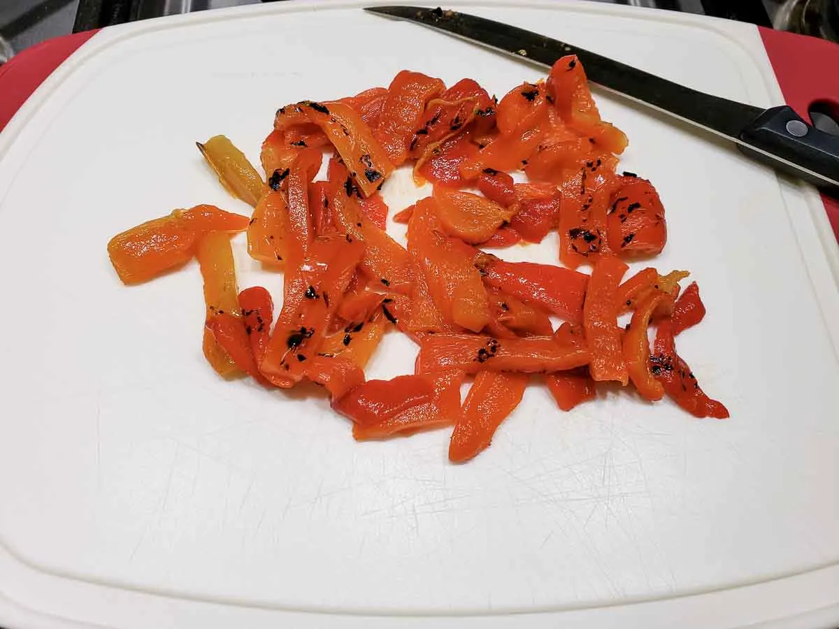 roasted red peppers sliced on a cutting board with a knife.