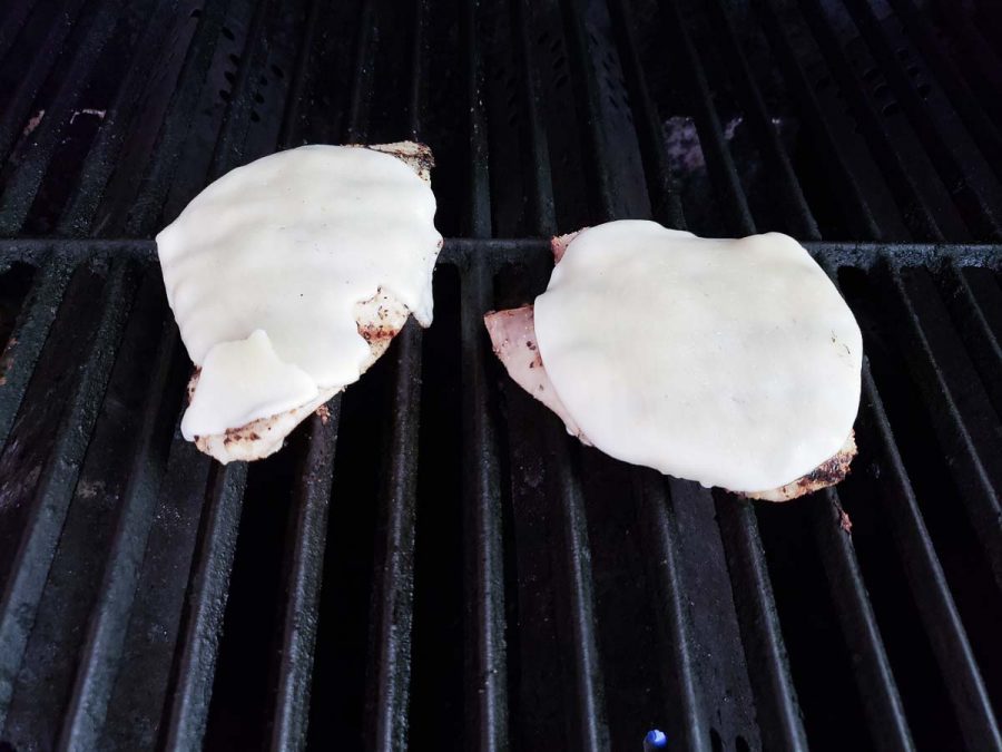 to chicken cutlets topped with provolone cheese cooking on a grill