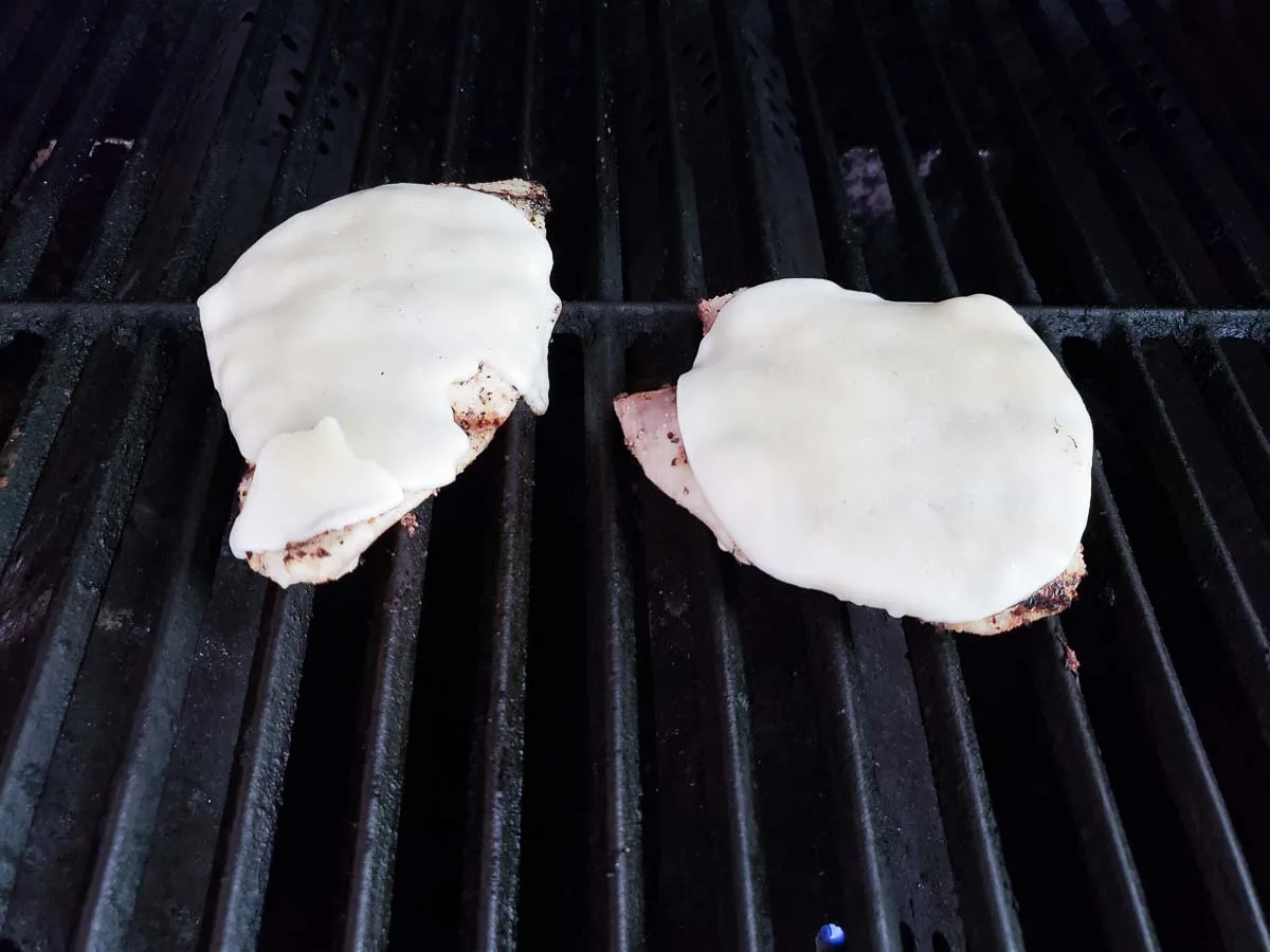 to chicken cutlets topped with provolone cheese cooking on a grill.
