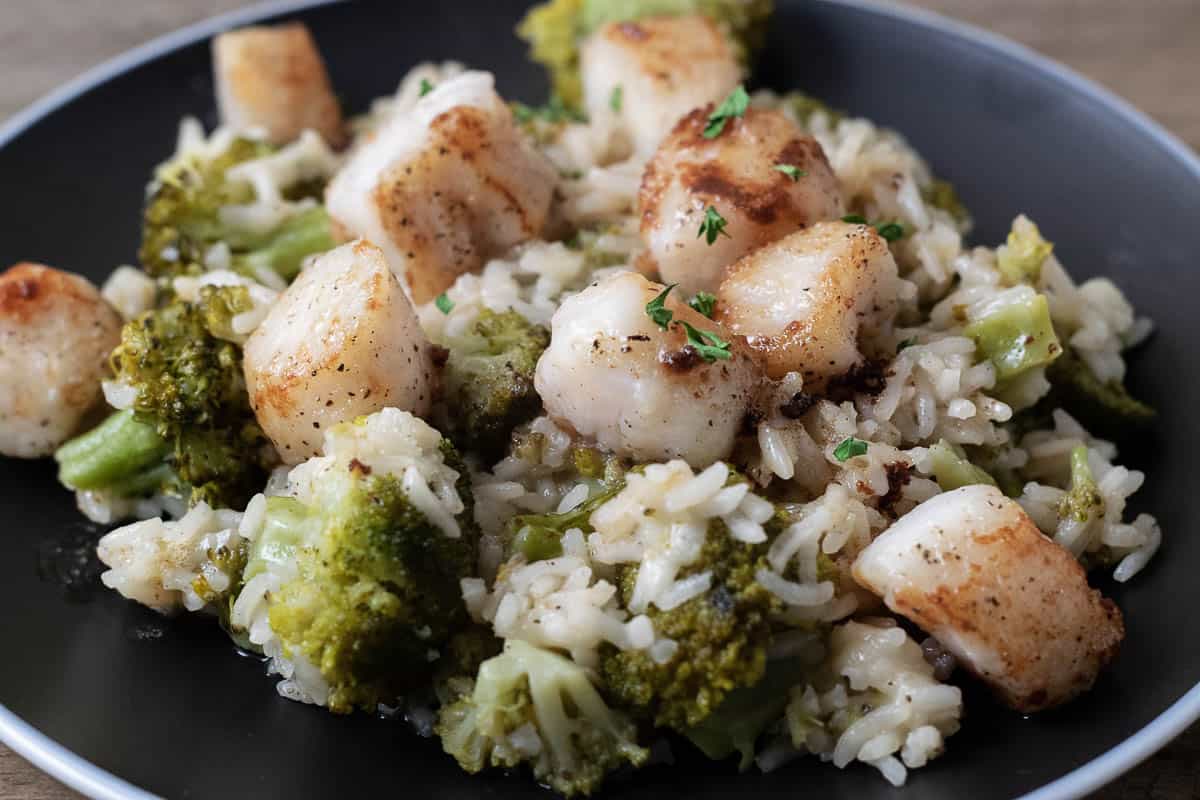 Scallops with Rice and Broccoli with parmesan cheese and brown butter drizzle on a plate.