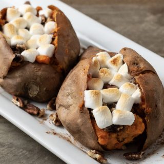 two marshmallow stuffed sweet potatoes with pecan streusel on a platter.