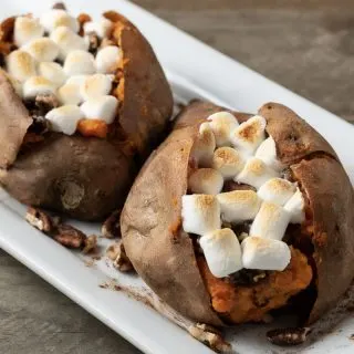 two marshmallow stuffed sweet potatoes with pecan streusel on a platter.