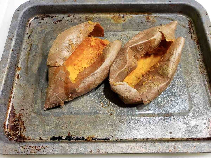 two sweet potatoes on a baking sheet with the flesh scooped out of the centers.