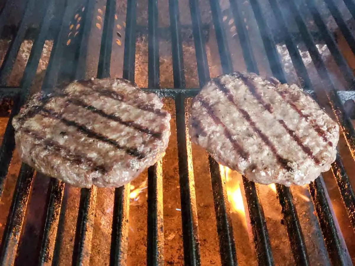 two burgers cooking on a gas grill.