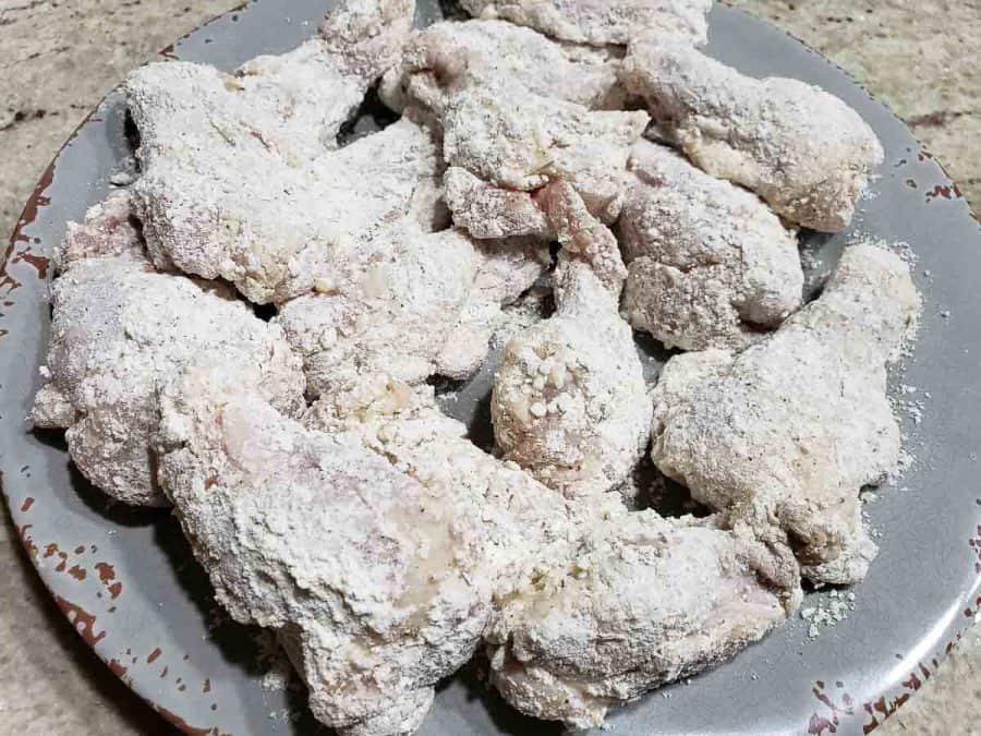 chicken wings coated in flour and crushed cracker mixture ready to be fried.