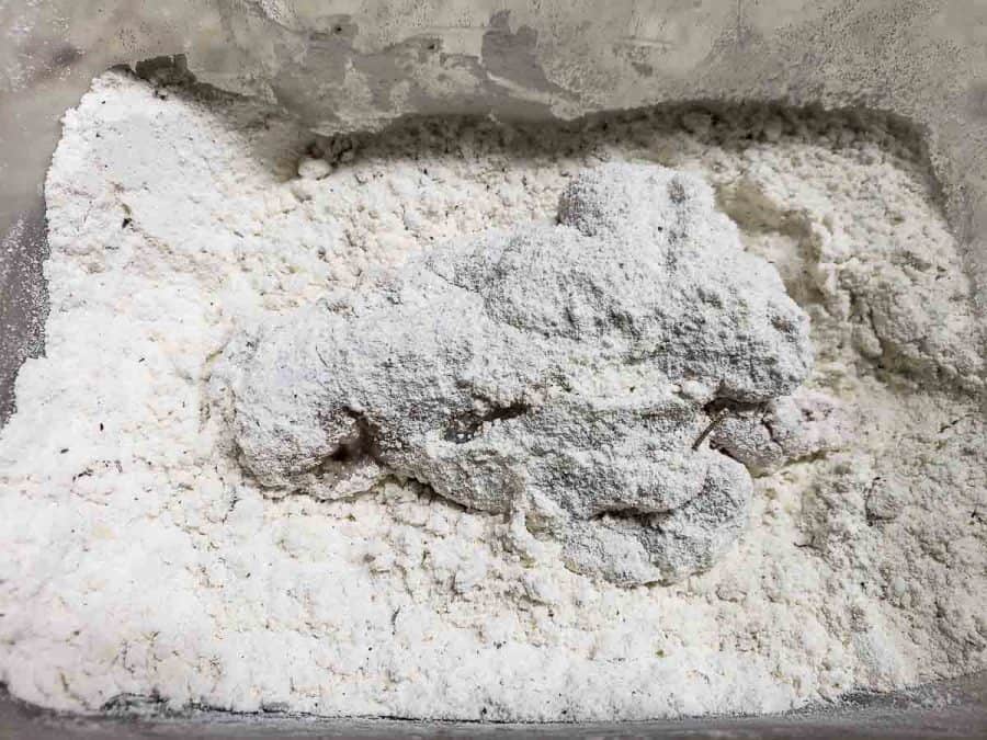 a chicken wing drummy getting coated in flour and crushed cracker mixture.