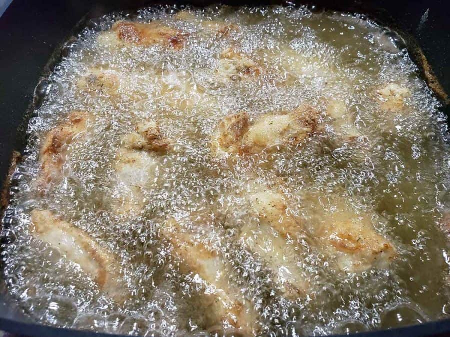 chicken wings and drummies deep frying in an electric skillet.