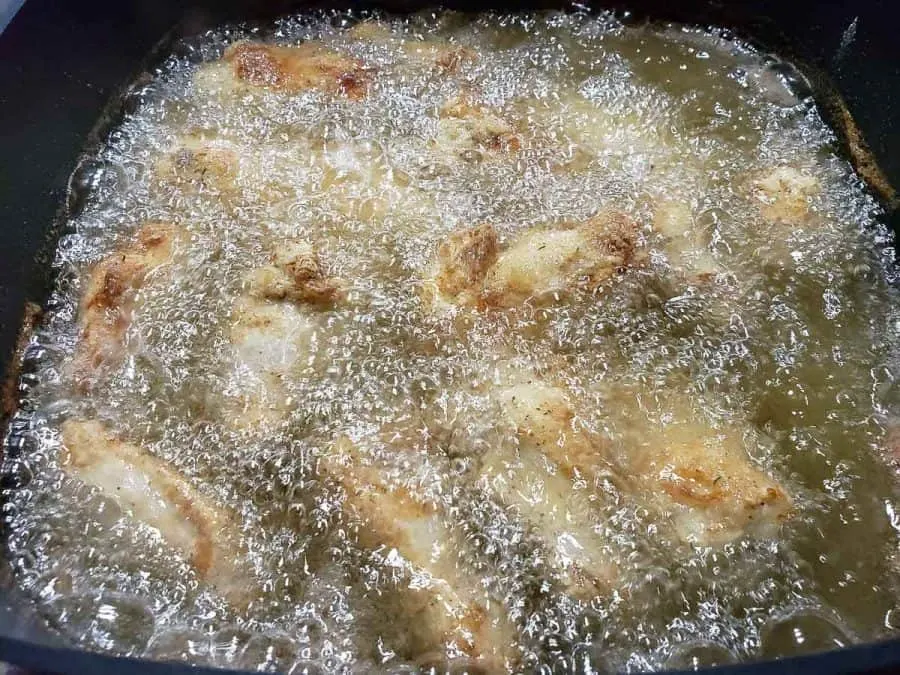 chicken wings and drummies deep frying in an electric skillet.