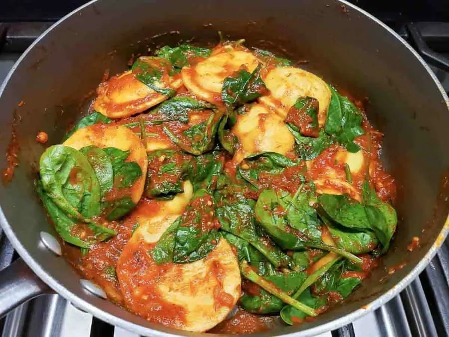 spinach, ravioli, and sauce cooking in a pan