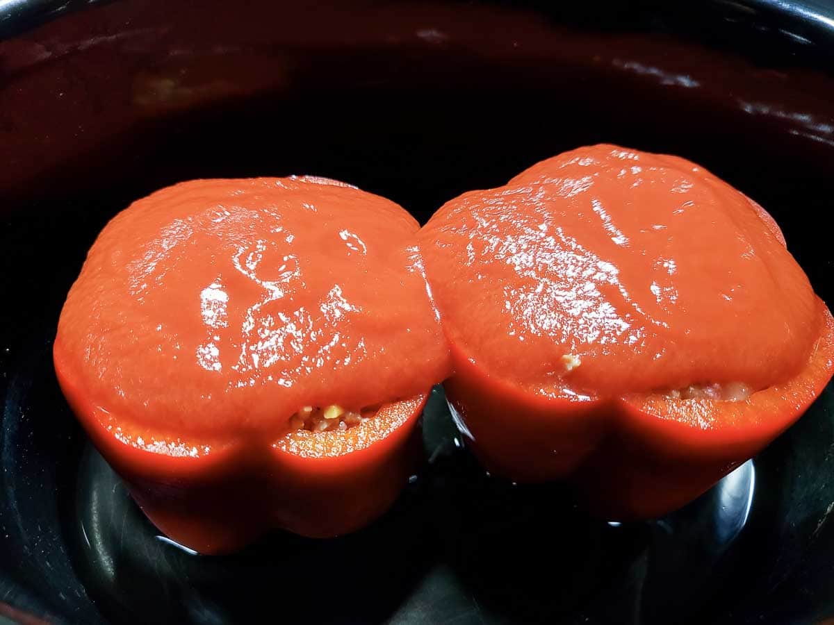 two Mexican stuffed peppers topped with tomato sauce in a slow cooker crockpot.