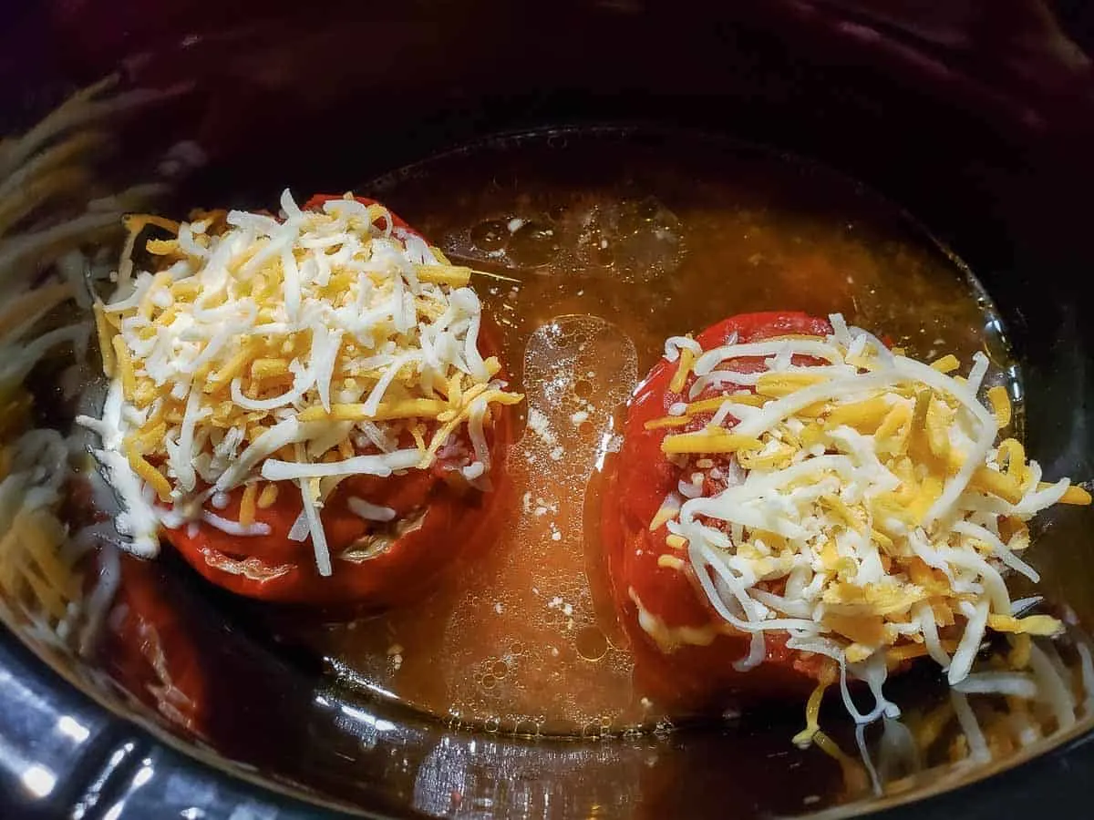 2 Mexican stuffed peppers topped with cheese in a slow cooker crock pot.