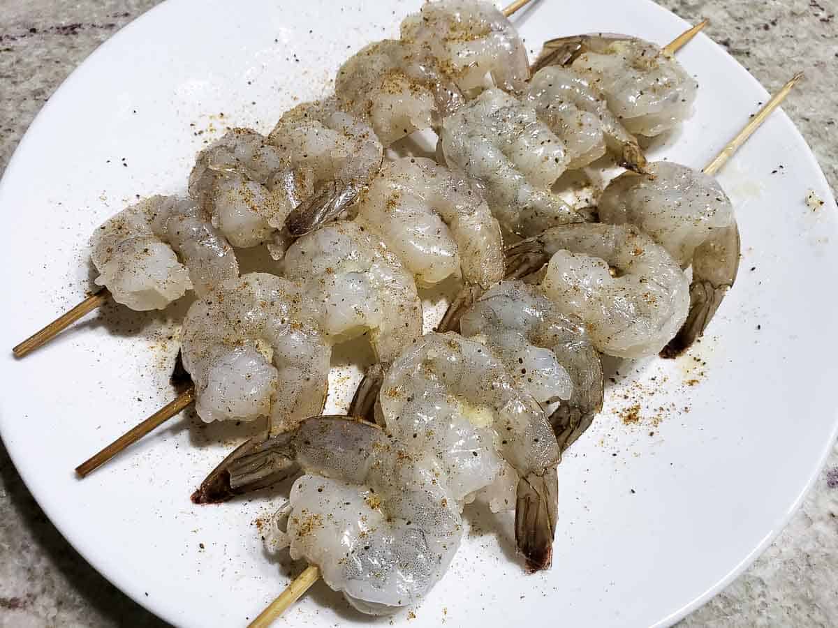 raw shrimp on skewers on a plate seasoned with old bay seasoning.