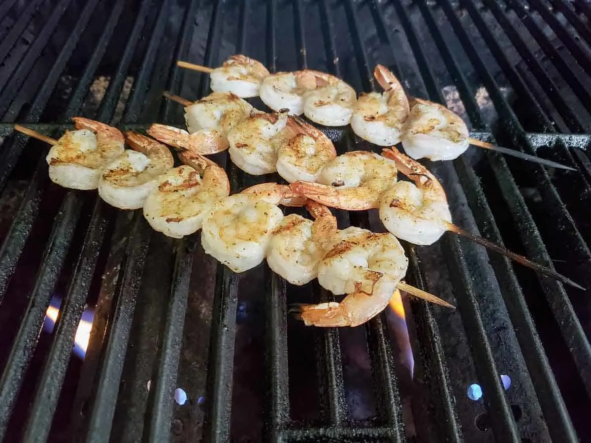 shrimp on skewers cooking on a gas grill.