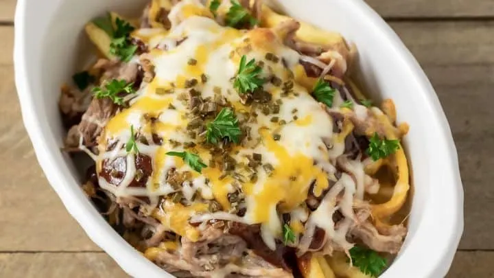 a baking dish filled with loaded bbq fries, Kalua pulled pork, and melted cheese
