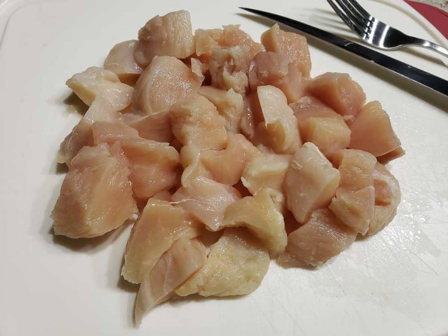 diced chicken on a cutting board with a knife and fork.