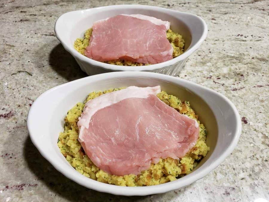 a pork chop layered over stuffing in two casserole baking dishes.