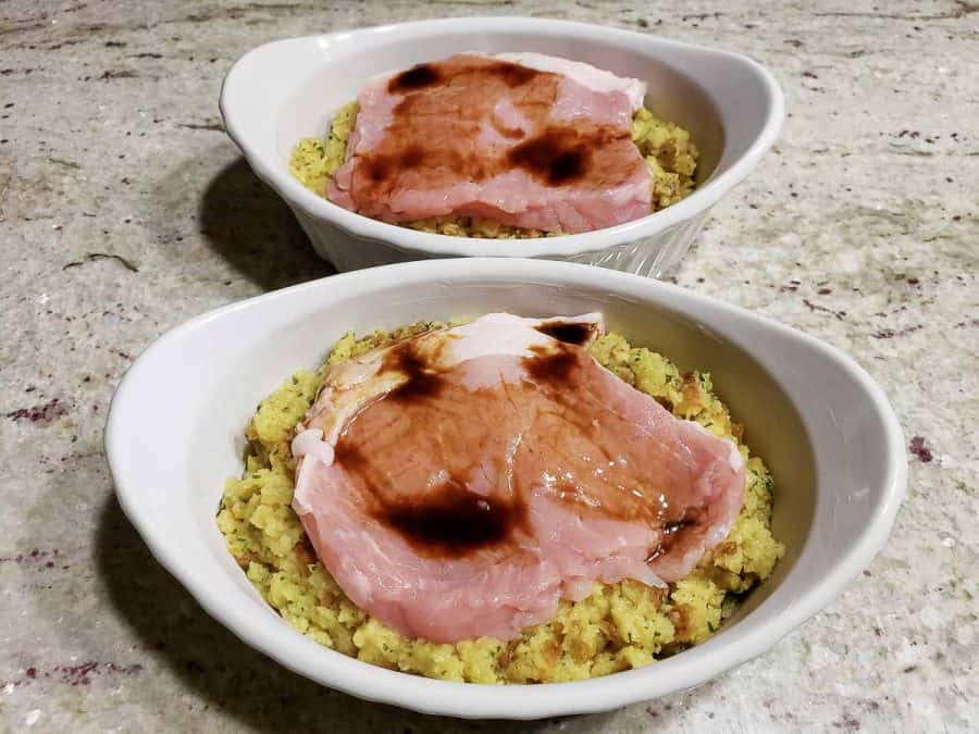 two casserole baking dishes filled with stuffing, pork chops, and topped with Worcestershire sauce.