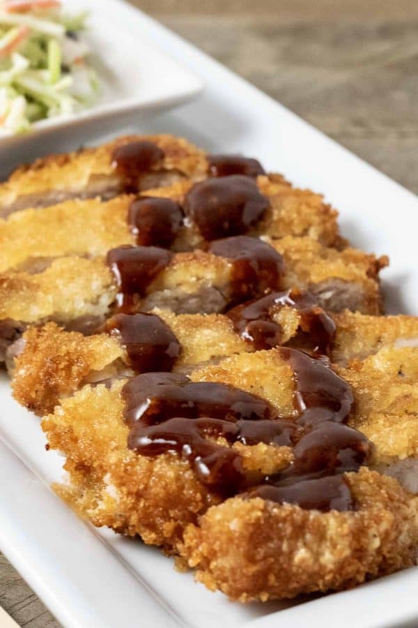 Japanese Fried Pork Cutlet on a plate with Homemade Tonkatsu Sauce drizzled on top.