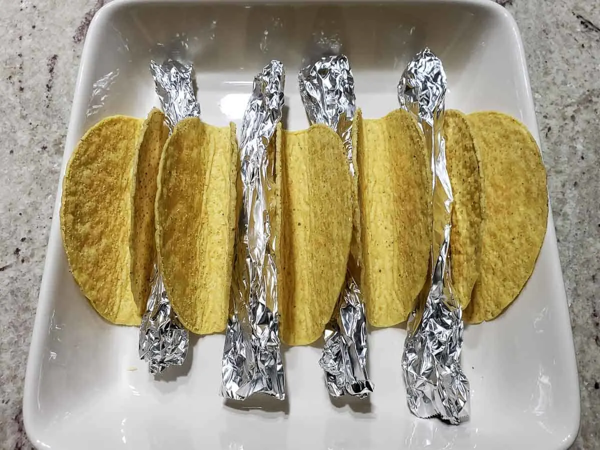 5 taco shells with rolled tinfoil in between in a baking dish
