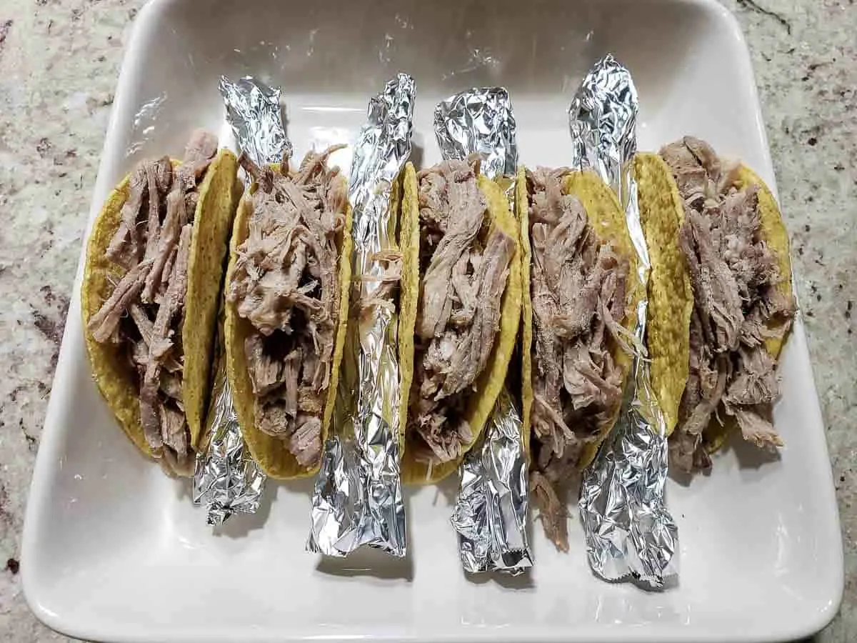 5 taco shells filled with pulled pork and rolled tinfoil in between in a baking dish