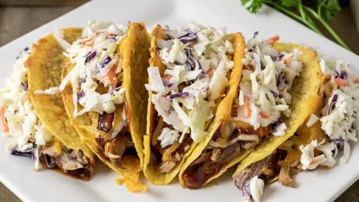 a platter filled with five Smoky BBQ Pulled Pork Tacos with Slaw