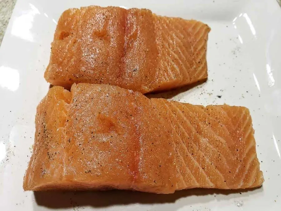 two salmon filets seasoned with salt and pepper on a plate.