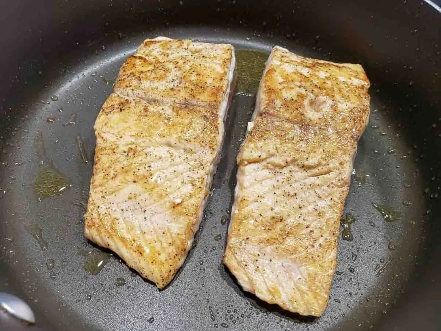 two salmon filets cooking in a frying pan.