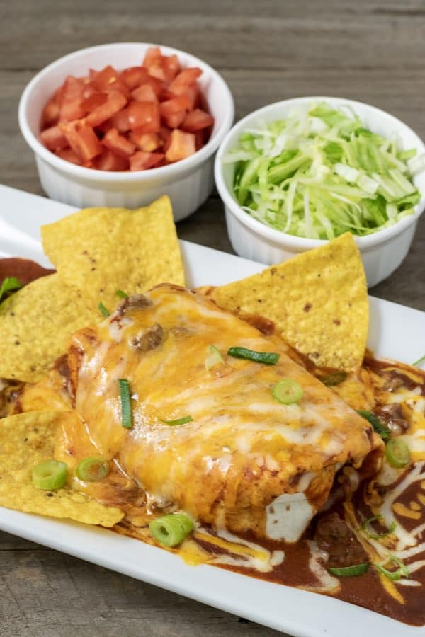 a wet burrito on a plate with sides of lettuce and tomato