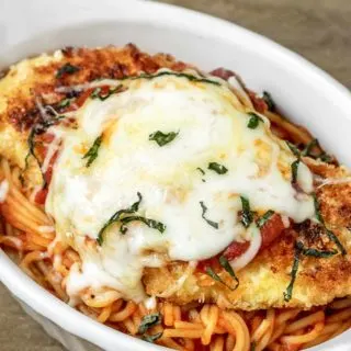 a baking dish filled with spaghetti topped with breaded fried chicken and melted mozzarella cheese