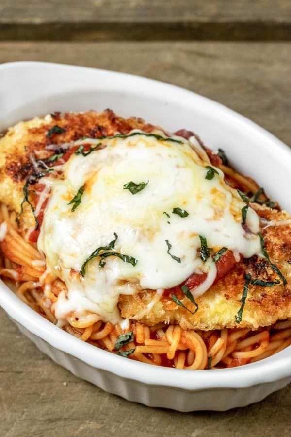 a baking dish filled with spaghetti topped with breaded fried chicken and melted mozzarella cheese