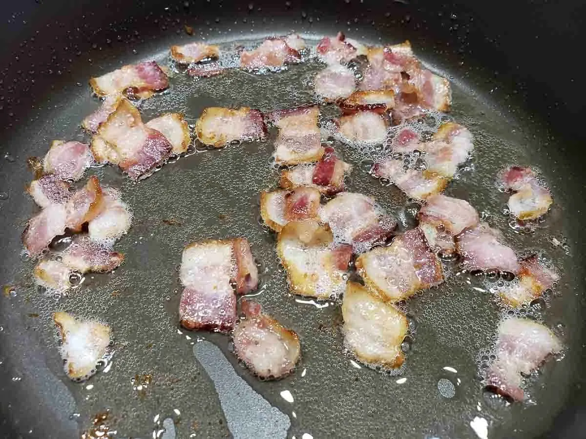 1 inch pieces of bacon frying in a pan.