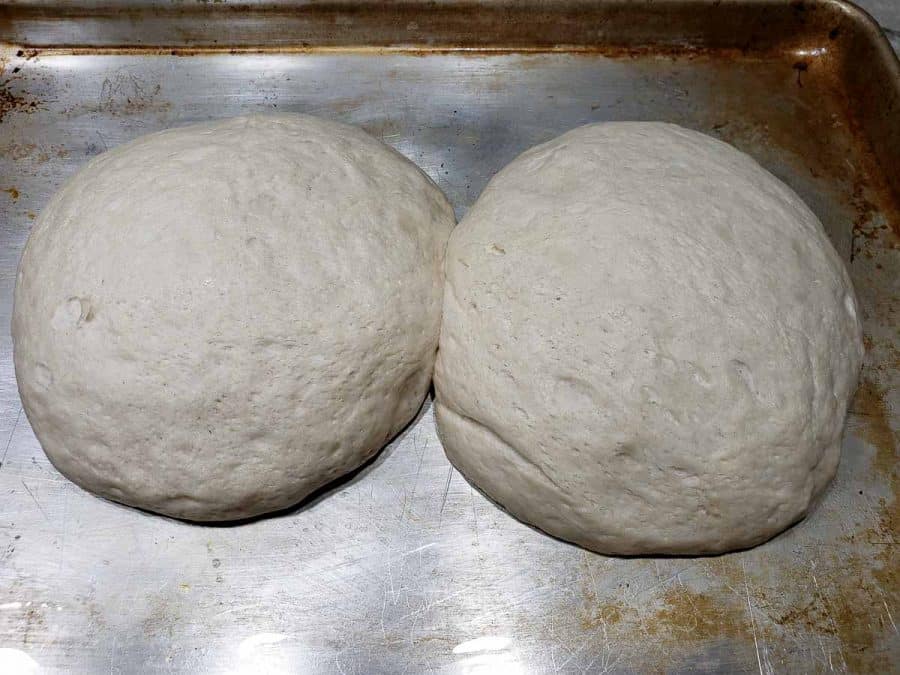 two risen round dough balls on a baking sheet