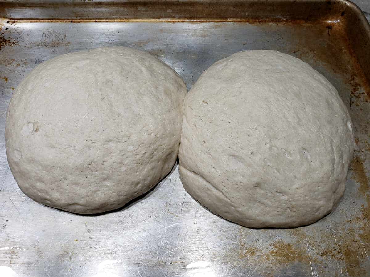 two risen round dough balls on a baking sheet.