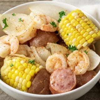 a bowl filled with shrimp, potatoes, onions, smoked sausage, and corn topped with old bay seasoning
