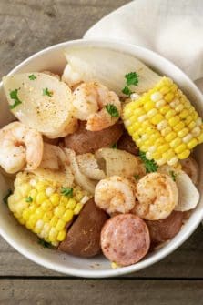 a bowl filled with shrimp, potatoes, onions, smoked sausage, and corn and sprinkled with old bay seasoning