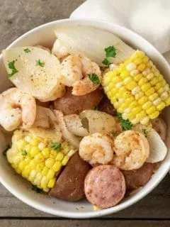 a bowl filled with shrimp, potatoes, onions, smoked sausage, and corn and sprinkled with old bay seasoning