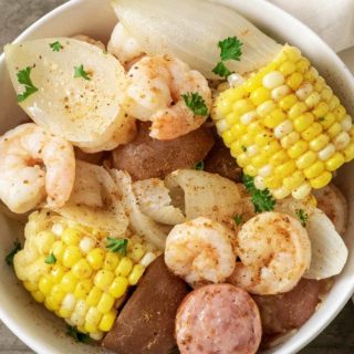 a bowl filled with shrimp, potatoes, onions, smoked sausage, and corn and sprinkled with old bay seasoning