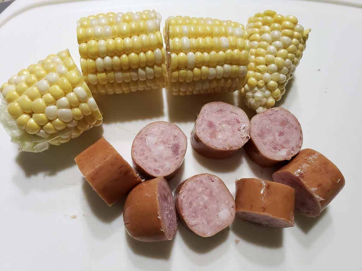 a corn on the cob cut into 4 pieces and diced smoked sausage on a cutting board.