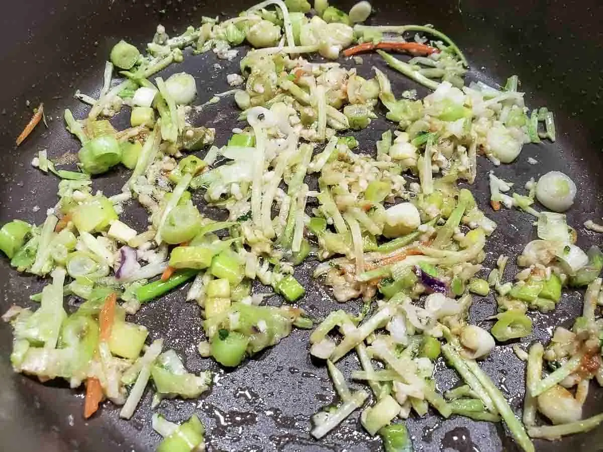 broccoli slaw and green onions cooking in a frying pan.