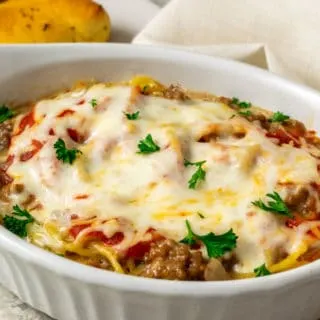 a baking dish filled with spaghetti noodles, ground beef, red sauce, and cheese and a side of bread sticks